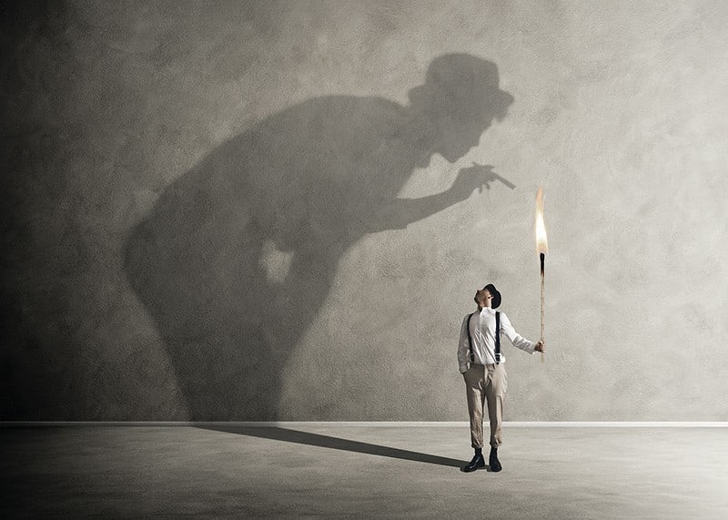 A symbolic image of facing one's inner demons, where a small torch casts a large, confrontational shadow-12