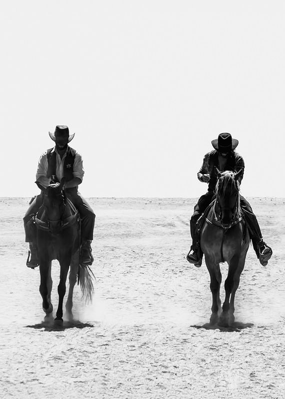 Doi cowboy călătoresc unul lângă altul printr-un peisaj pustiu, încadrat de misterul atemporal și libertatea Vestului Sălbatic.-12
