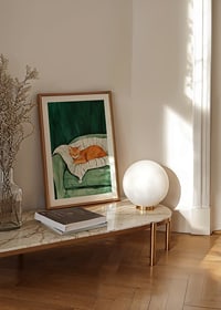 A poster with a sleeping orange cat on a striped blanket in a green armchair-8